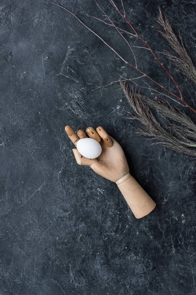 Рука манекена с куриным яйцом на тёмном фоне — стоковое фото