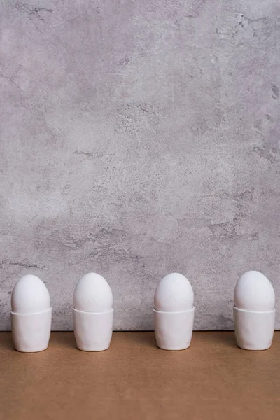 Fila de ovos brancos em copos sobre fundo cinzento — Fotografia de Stock