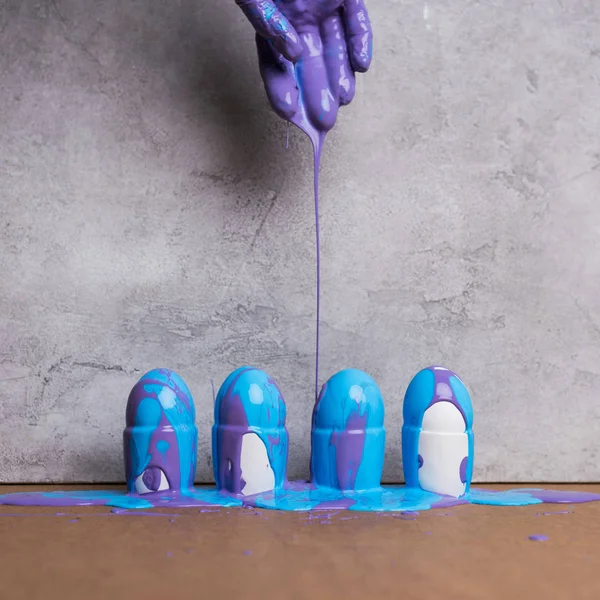 Hand pouring paint on eggs in cups on grey background — Stock Photo