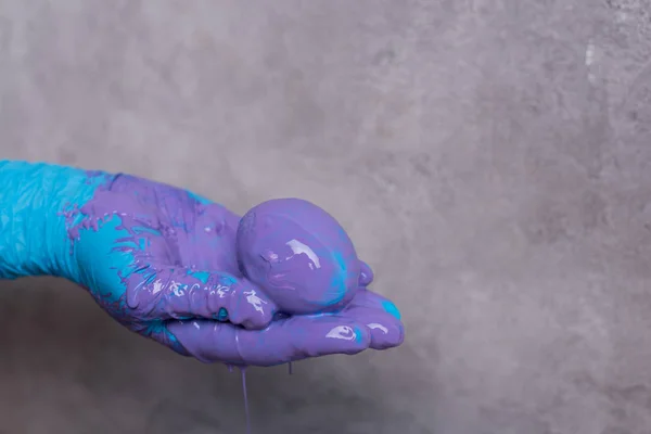 Hand in glove holding egg in paint — Stock Photo