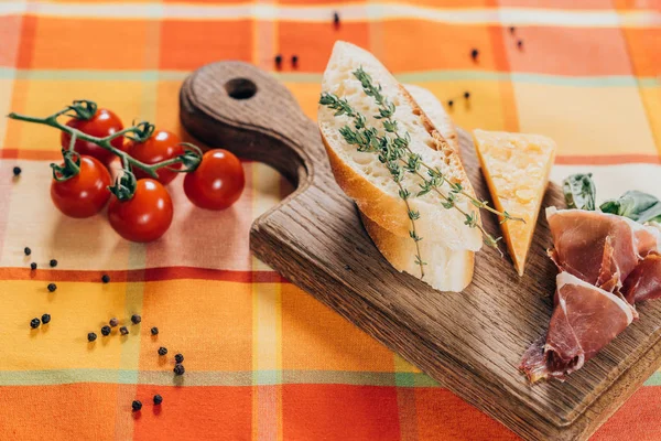 Top view of sliced baguette, meat and parmesan cheese on wooden cutting board and fresh cherry tomatoes on table top — Stock Photo
