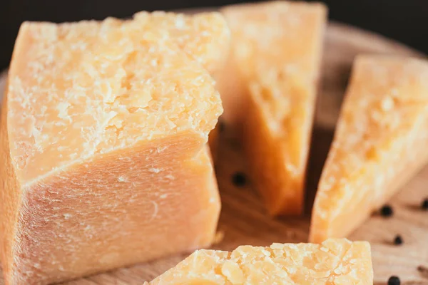 Vista de cerca del queso parmesano gourmet con granos de pimienta en la tabla de cortar de madera - foto de stock