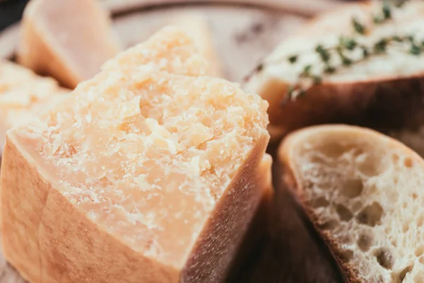 Vista de cerca del queso parmesano gourmet y rebanadas de pan fresco en la tabla de cortar de madera - foto de stock