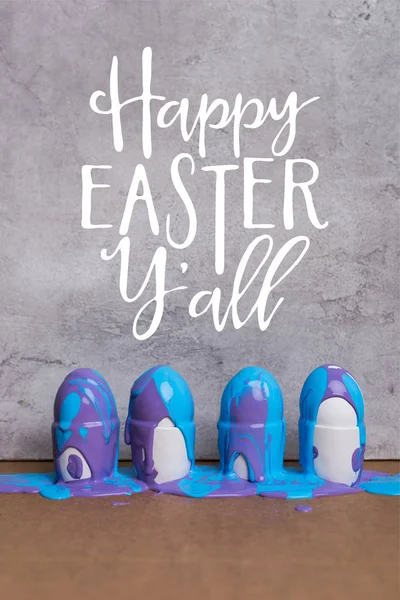 Eier in Tassen mit fröhlichem Osterschriftzug auf grauem Hintergrund bemalen — Stockfoto