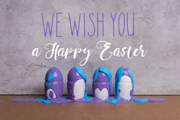 Paint covering eggs in cups with we wish you happy easter lettering on grey background — Stock Photo