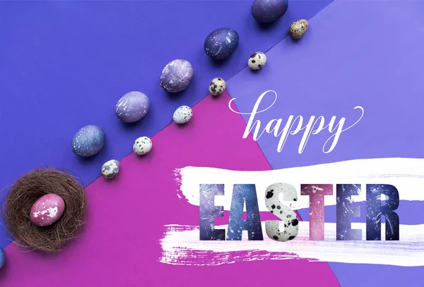 Rows of painted chicken and quail eggs and nest with happy easter lettering on background in purple tones — Stock Photo