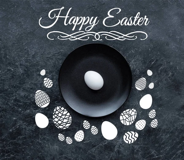 Huevo blanco en plato negro con letras de Pascua feliz y huevos dibujados sobre fondo oscuro - foto de stock