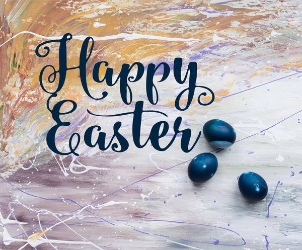 Painted Easter eggs with happy easter lettering on stained background — Stock Photo