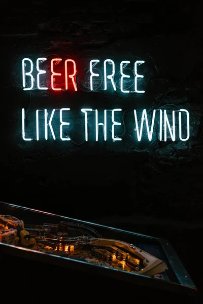 Birra gratis come il vento iscrizione al neon sul muro scuro e gioco da tavolo nel pub — Foto stock