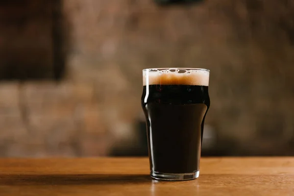 Glass of fresh cold dark beer on wooden table in pub — Stock Photo