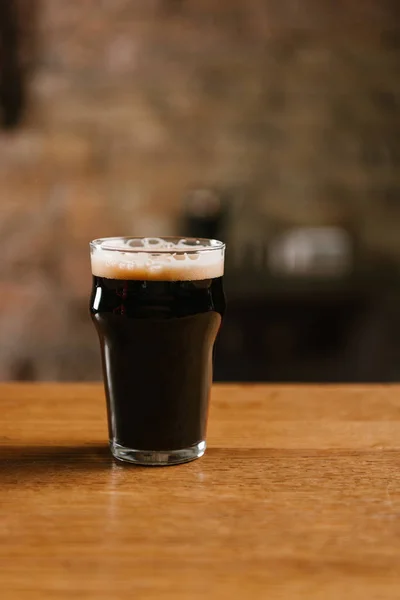 Fresh cold dark beer with foam in glass on wooden table in pub — Stock Photo