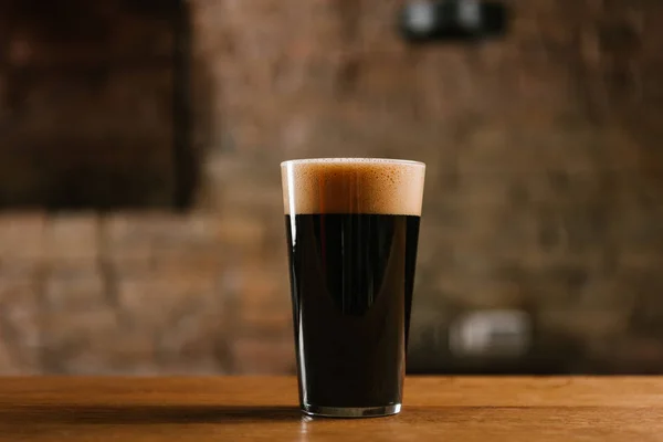 Vista de cerca de la cerveza fría fresca con espuma en vidrio sobre mesa de madera - foto de stock