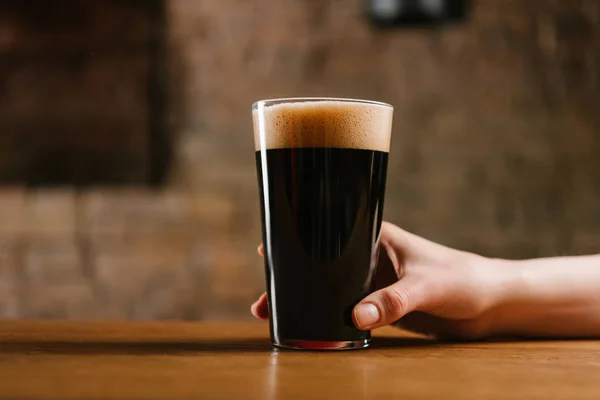 Chupito de mano con vaso de cerveza fresca y oscura en el pub - foto de stock