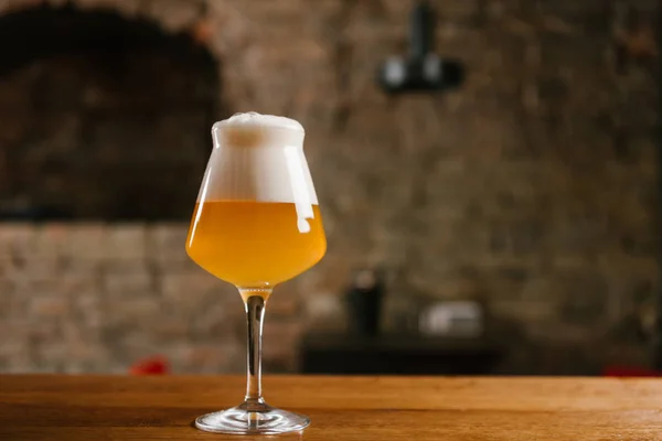 Cold beer with foam in glass on wooden table in pub — Stock Photo