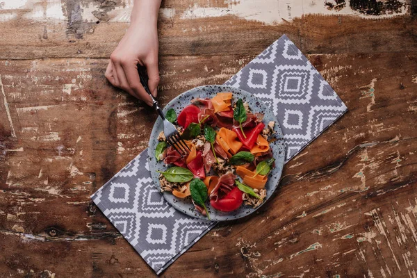 Cropped shot of human hand holding fork and delicious salad with mussels, vegetables and jamon — Stock Photo