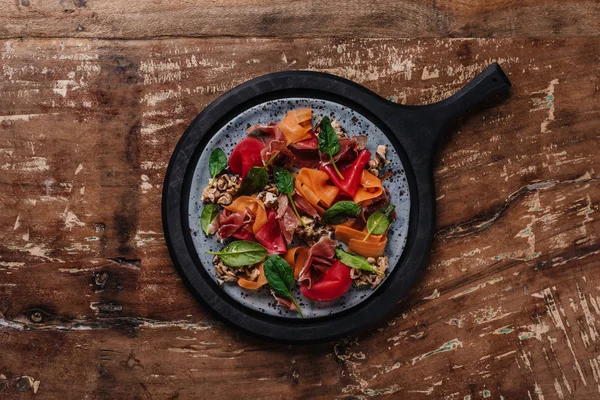 Вид на свежий вкусный салат с мидиями, корнеплодами и хамоном на деревянном столе — стоковое фото