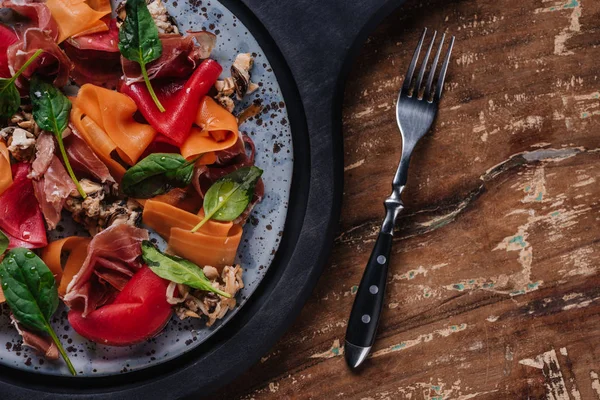 Ensalada gourmet fresca con mejillones, verduras y jamón en el plato y tenedor en la mesa de madera - foto de stock