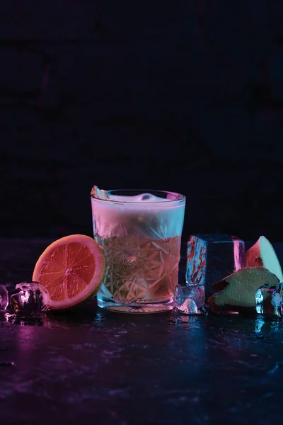 Vaso con cóctel de uñas de jengibre y cubitos de hielo de fusión en la superficie oscura - foto de stock