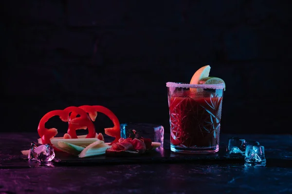 Вкусный кровавый коктейль из стекла и овощей с тающими кубиками льда на темной поверхности — стоковое фото