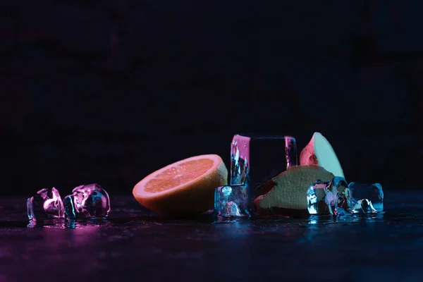 Primo piano vista di sciogliere cubetti di ghiaccio, limone affettato e zenzero sulla superficie scura — Foto stock