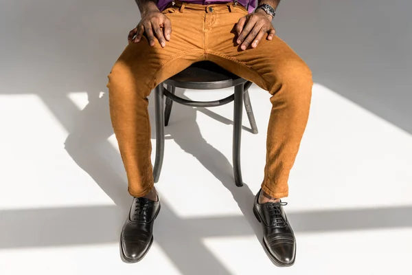 Schnappschuss eines afrikanisch-amerikanischen Mannes in stilvoller Kleidung, der auf einem Stuhl auf grauem Hintergrund sitzt — Stockfoto