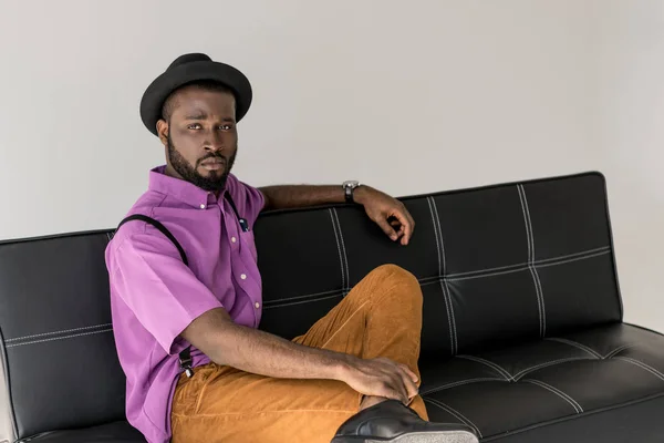 Thoughtful african american fashionable man resting on black sofa isolated on grey — Stock Photo