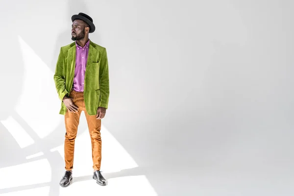 Вдумчивый африканский американец в модной одежде и шляпе позирует на сером фоне — стоковое фото