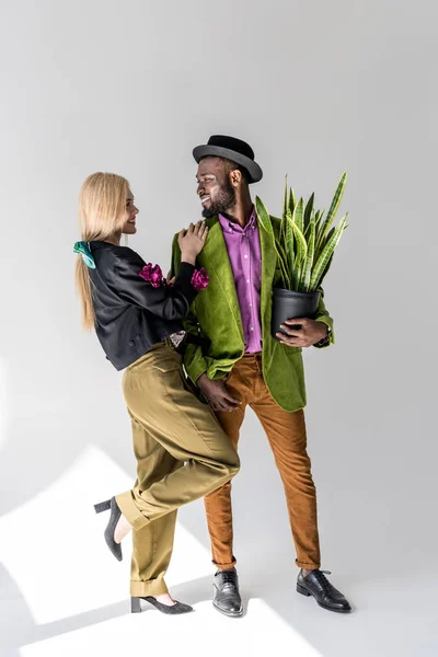 Sourire interracial couple élégant avec plante verte en pot de fleurs posant sur fond gris — Photo de stock