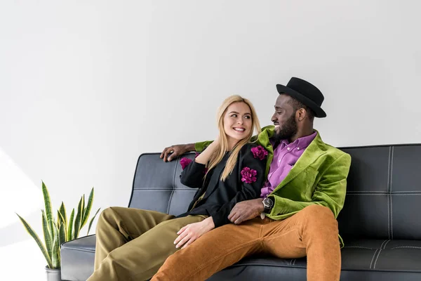 Портрет усміхненої мультикультурної модної пари, що відпочиває на чорному дивані — стокове фото