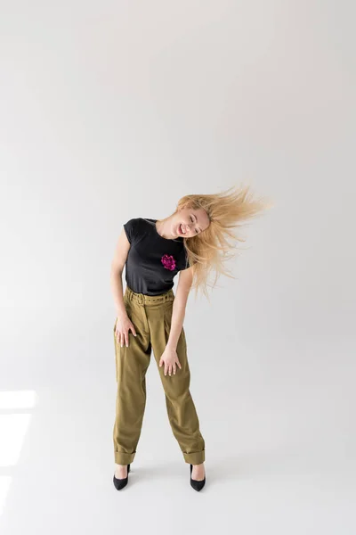 Volle Länge Ansicht der fröhlichen blonden Mädchen tanzen und schütteln Haare auf grau — Stockfoto