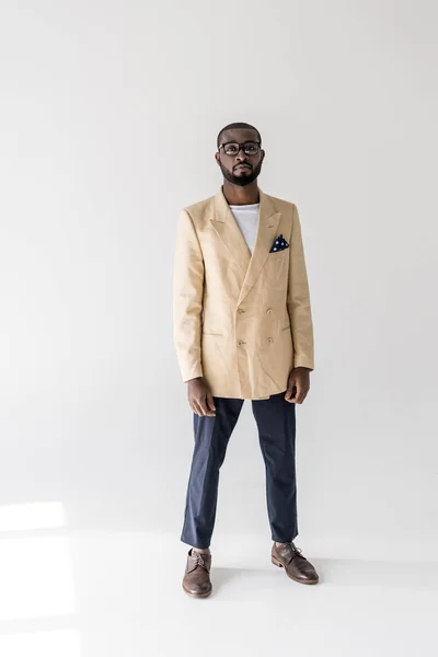 Full length view of handsome young african american man in eyeglasses and fashionable clothes looking at camera on grey — Stock Photo