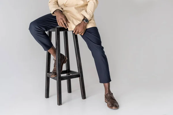 Abgeschnittene Aufnahme von stilvollen afrikanisch-amerikanischen Mann sitzt auf Stuhl isoliert auf grau — Stockfoto