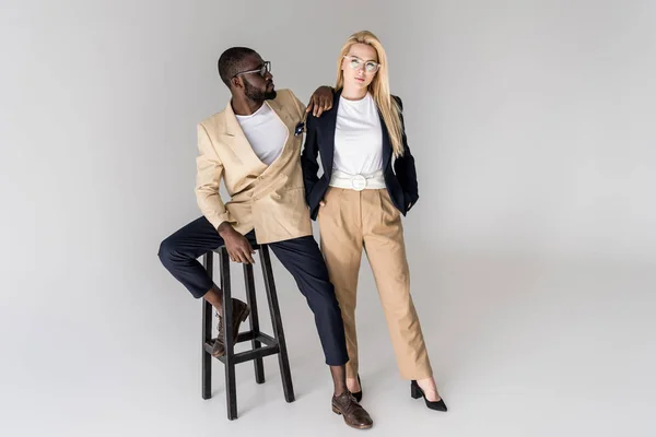 Vista completa de la elegante pareja joven multiétnica en gafas posando juntos aislados en gris - foto de stock