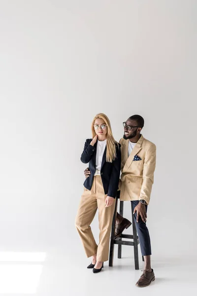 Beautiful fashionable young multiethnic couple in spectacles posing together on grey — Stock Photo