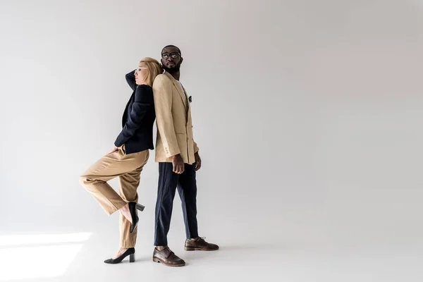 Side view of fashionable young multiethnic couple posing back to back on grey — Stock Photo