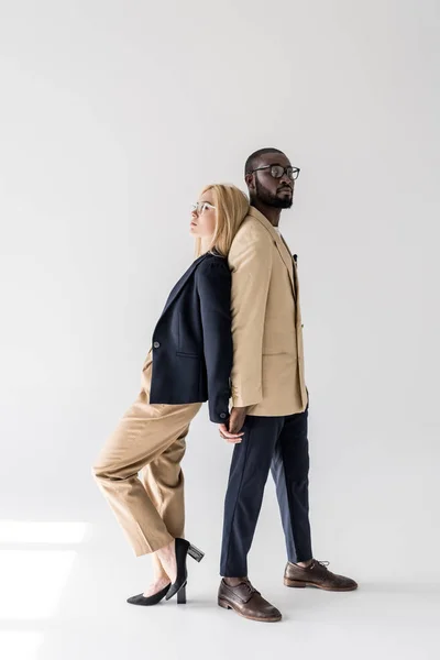 Vista laterale di elegante giovane coppia multietnica in piedi schiena a schiena e tenendo le mani sul grigio — Foto stock