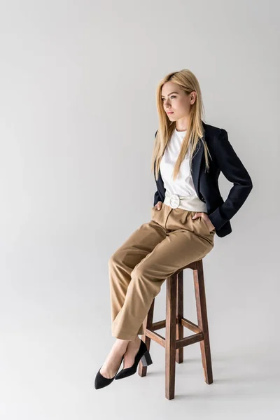 Vue pleine longueur de belle fille blonde élégante assise sur une chaise et regardant loin isolé sur gris — Photo de stock