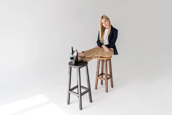 Красивая стильная молодая женщина сидит на стульях и смотрит в камеру на сером — стоковое фото
