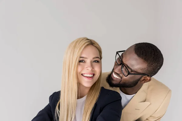 Happy young african american man in eyeglasses lookign at beautiful blonde girlfriend isolated on grey — Stock Photo