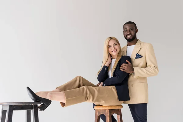 Alegre elegante joven pareja multiétnica sonriendo a la cámara aislada en gris - foto de stock