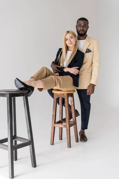 Belo elegante jovem casal multiétnico posando juntos e olhando para a câmera no cinza — Fotografia de Stock