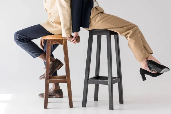 Cropped shot of multiethnic couple sitting back to back on stools and holding hands on grey — Stock Photo