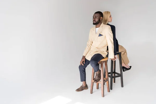 Vista de ángulo alto de la pareja multiétnica joven de moda sentado espalda con espalda en gris - foto de stock