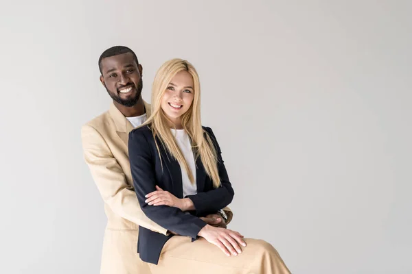Glückliche junge multiethnische Paar umarmt und lächelt in die Kamera isoliert auf grau — Stockfoto