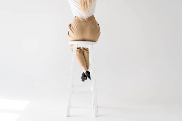 Plan recadré de fille blonde assise sur un tabouret sur du gris — Photo de stock