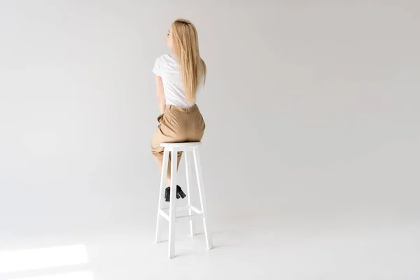 Rückseite der stilvollen blonden Frau sitzt auf einem Schemel auf grau — Stockfoto