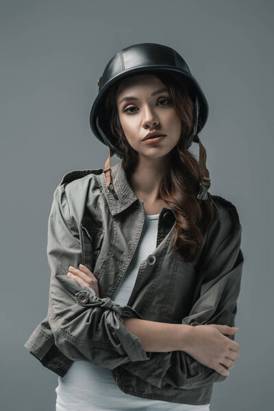 beautiful girl posing in military helmet with crossed arms, isolated on grey