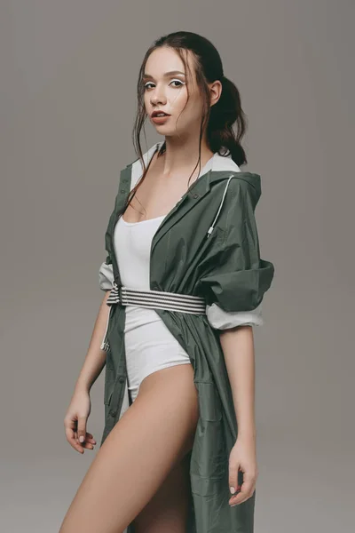 Attractive young girl posing in bodysuit and raincoat, isolated on grey — Stock Photo