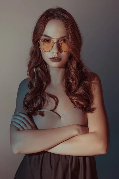 Schönes Mädchen mit gelber Sonnenbrille posiert mit verschränkten Armen, isoliert auf grau — Stockfoto