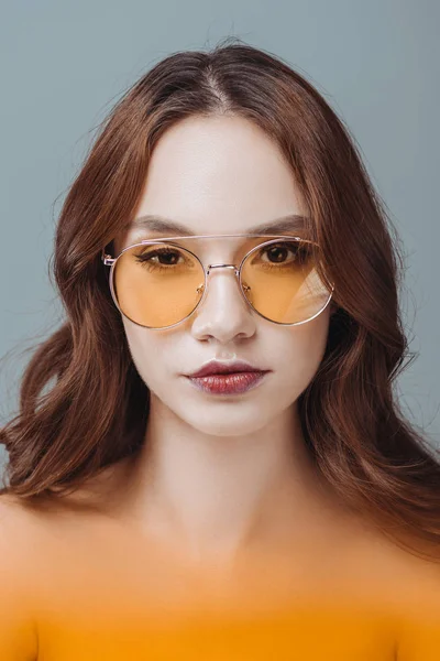 Красива молода дівчина позує в жовтих сонцезахисних окулярах, ізольована на сірому — стокове фото